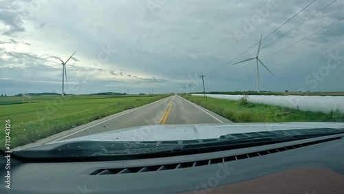 POV - driving on country road past hay fields  with wrapped bales, corn fields and  wind turbines; clouds heavy with rain in early fall in Midwest; concepts of green energy, farming and rural life photo