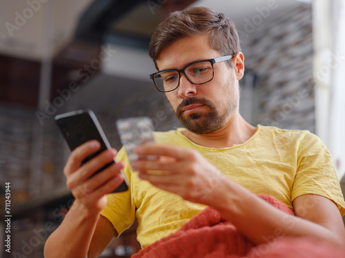 Young Caucasian man using smart phone for reading, searching prescription on bottle medicine, pill label text about information online, instructions side effects, pharmacy medicament concept photo