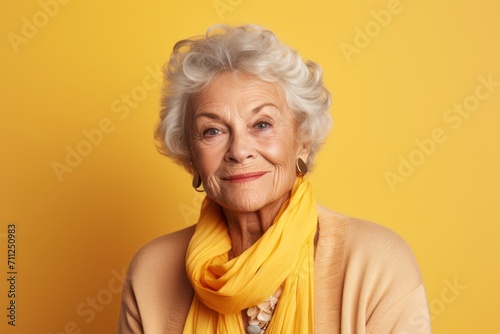 Portrait of happy senior woman with yellow scarf on yellow background.