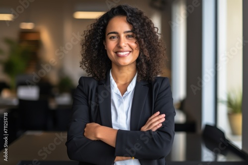 Empowered businesswoman inside an office with arms folded and a subdued smile 