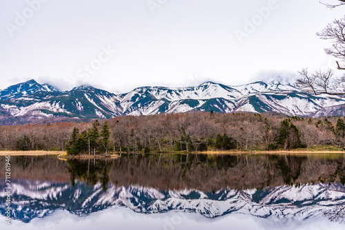 Small islet in the lake  beautiful lake surface reflecting blue sky like a mirror  rolling mountain range and woodland in the background on springtime sunny day. High latitude country natural scenery