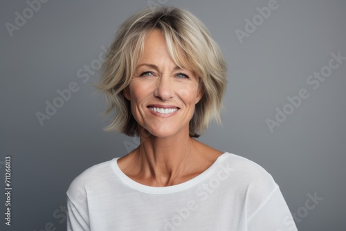 Portrait of a beautiful mature woman smiling while standing against grey background © Inigo