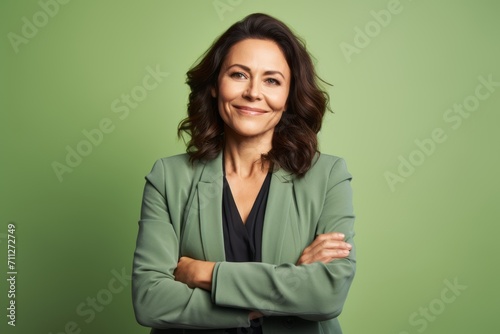 Portrait of mature business woman with crossed arms against green background.
