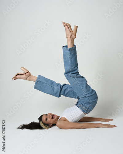 Full length portrait of brunette female asian model wearing casual clothes, white singlet shirt, denim jean pants. Sitting pose, side down with legs in air.  high camera angle for perspective. photo