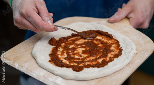 Kucharz w pizzerii smaruje spód pizzy sosem pomidorowym