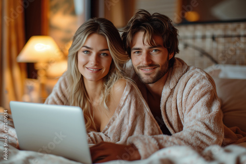 young couple in pajamas on bed with laptop photo