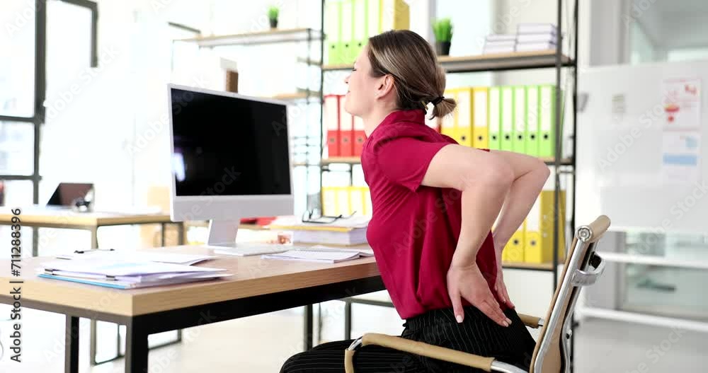 Woman sitting at desk with computer and holding on to lower back 4k movie slow motion. Sedentary lifestyle problems with spine concept