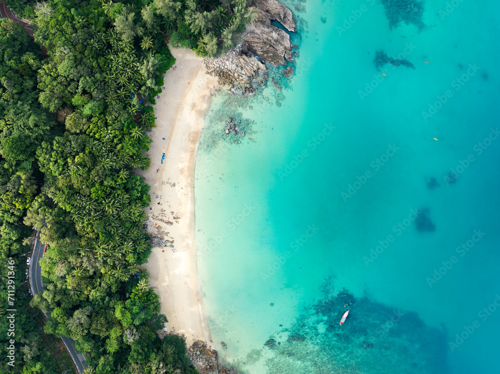View from above, stunning aerial view of Banana beach, a beautiful white sand beach surrounded by palm trees and bathed by a turquoise water. Phuket, Thailand.