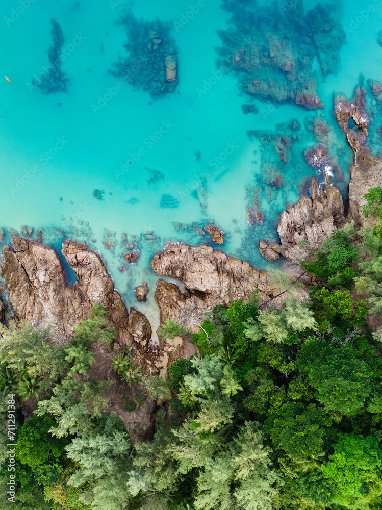 View from above, stunning aerial view of a rocky coastline surrounded by palm trees and bathed by a turquoise water. Phuket, Thailand.