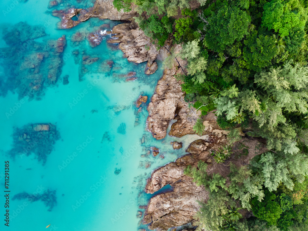 View from above, stunning aerial view of a rocky coastline surrounded by palm trees and bathed by a turquoise water. Phuket, Thailand.