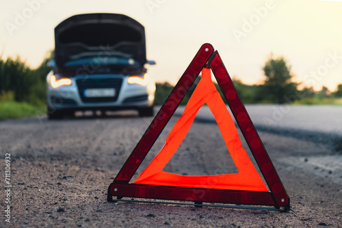 Broken silver luxury car emergency accident. Man driver installing red triangle stop sign on road. Sport automobile turned on blinkers technical problems on the road. Safety procedure when having