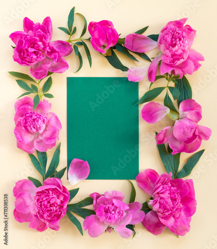 Garland of beautiful pink peonies on yellow paper background with postcard for congratulations or invitations. Creative floral wreath. Greeting card for holiday.