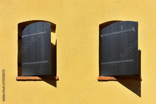 Facade of the historic building with yellow wall and small windows with wooden shutters open. Ancient architecture, rustic style. Torun, Poland, August 2023