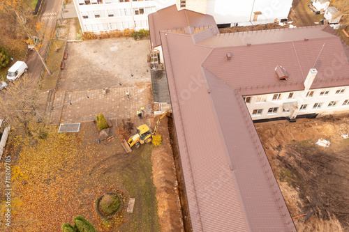 Drone photography of heavy machinery digging dirt around schools foundation and repairing it during autumn day