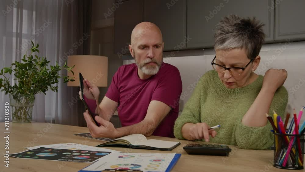 Focused attractive mature couple managing household finance, working with digital tablet , calculating expenses with calculator and planning family budget together at home. Focused attractive mature couple managing household finance, working with digital tablet , calculating expenses with calculator and planning family budget together at home.