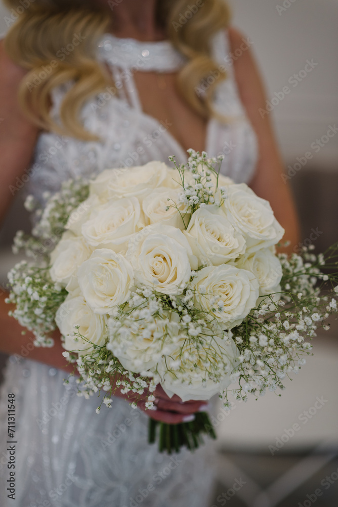 Bride in an elegant dress holds a vintage bouquet on ceremony. The bouquet with white flowers, roses, gypsophila and decorative plants. Wedding day. Beautiful bride portrait indoors. Closeup.