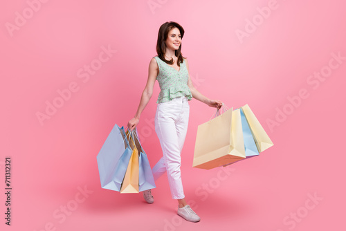 Full length photo of adorable cute girl wear summer clothes hold bags going shopping look empty space isolated on pink color background