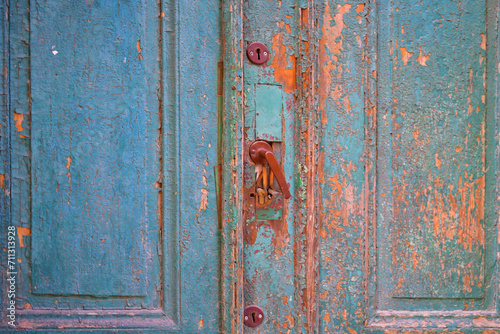 Old blue wooden door with cracks and fallen paint, with a metal handle and details. Grunge texture. Torun, Poland, August 2023