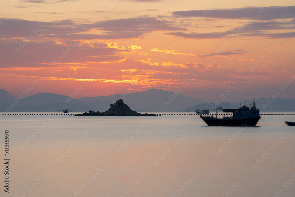 sunset landscape with sea, boat, island and clouds, long exposure
