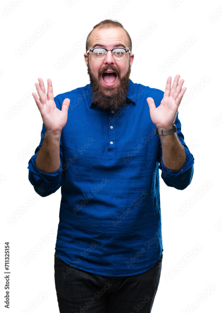Fototapeta premium Young caucasian hipster man wearing glasses over isolated background celebrating crazy and amazed for success with arms raised and open eyes screaming excited. Winner concept