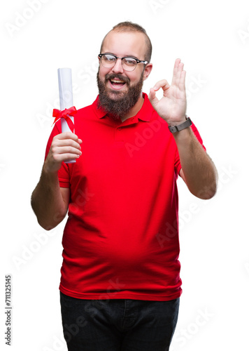 Young hipster man wearing glasses and holding degree over isolated background doing ok sign with fingers, excellent symbol