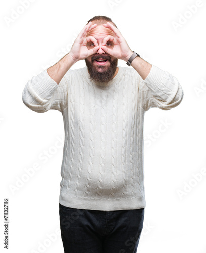 Young caucasian hipster man wearing winter sweater over isolated background doing ok gesture like binoculars sticking tongue out, eyes looking through fingers. Crazy expression.