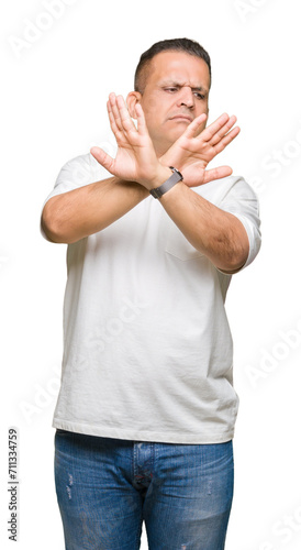 Middle age arab man wearig white t-shirt over isolated background Rejection expression crossing arms and palms doing negative sign, angry face photo