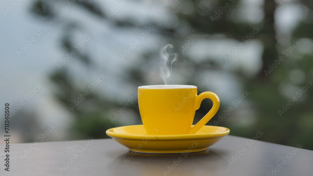 yellow coffee cup In the morning, a coffee cup is placed on the table in the background of a natural view.