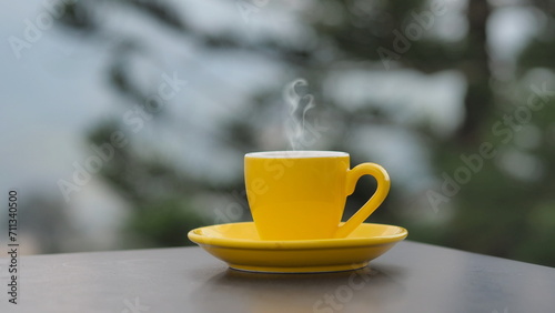 yellow coffee cup In the morning, a coffee cup is placed on the table in the background of a natural view.