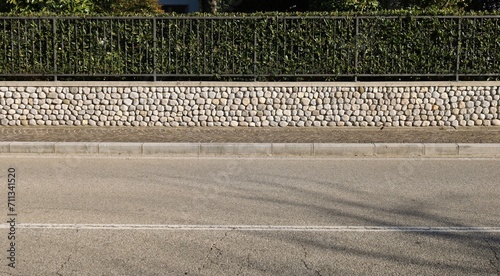 Fence made of low stone wall with railing on top and hedge behind. Sidewalk and urban street in front. Background for copy space photo