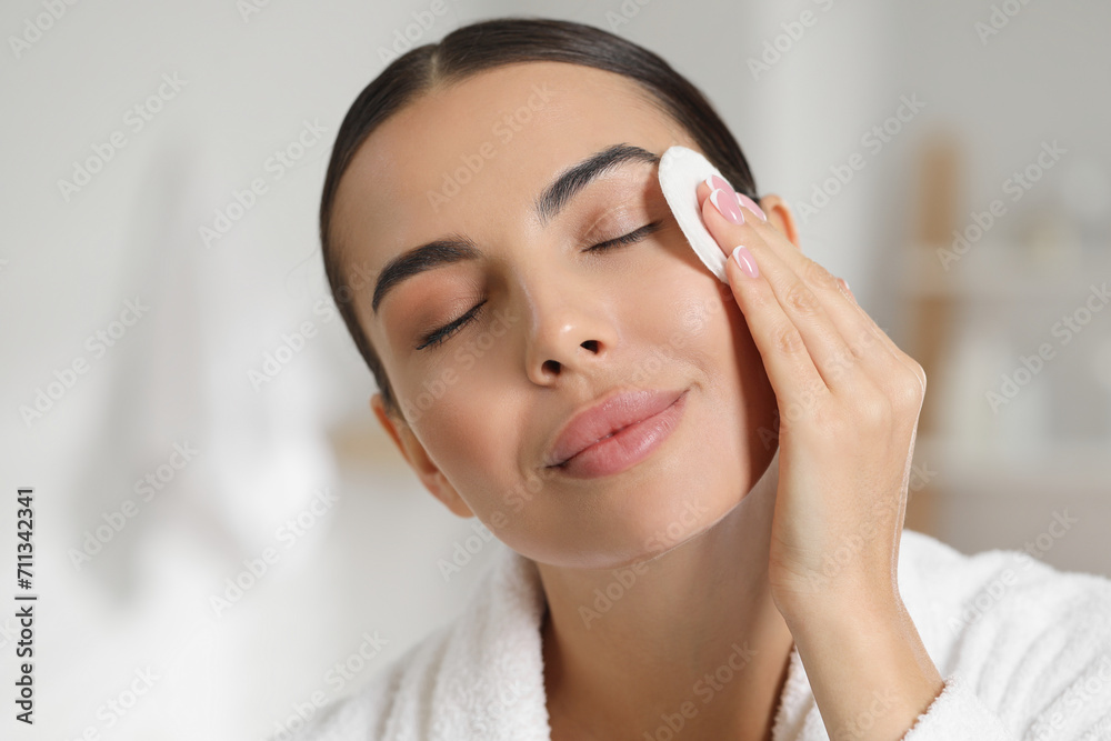 Beautiful woman removing makeup with cotton pad indoors