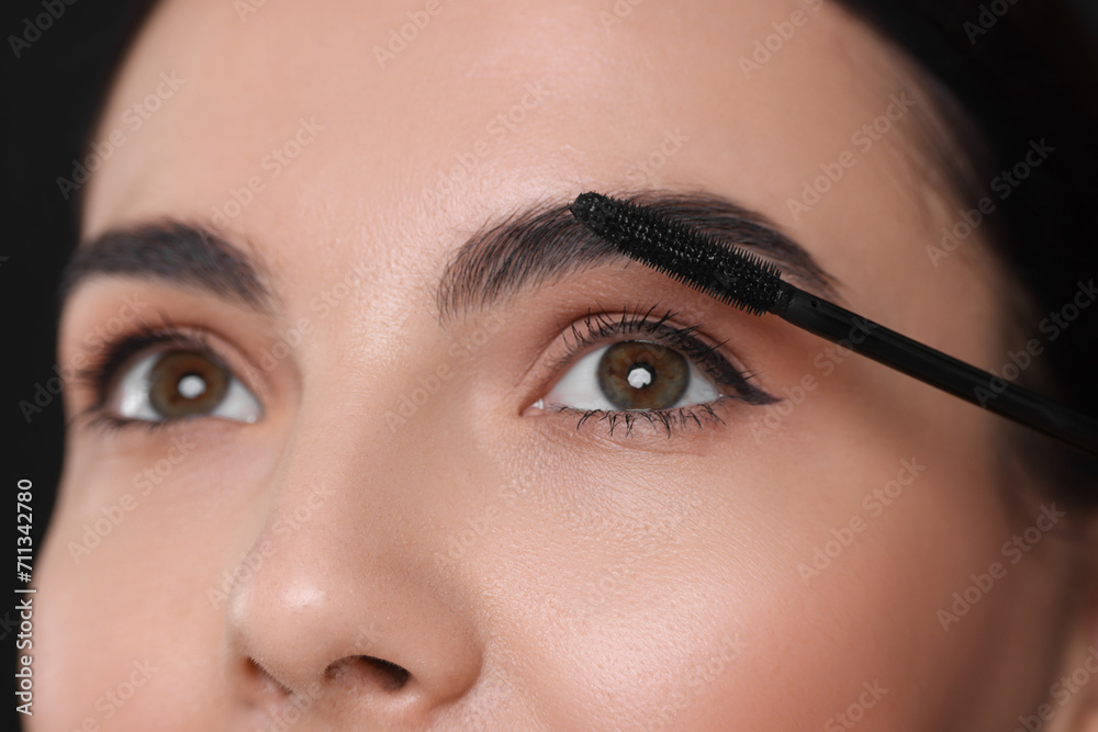 Beautiful young woman applying mascara on black background, closeup