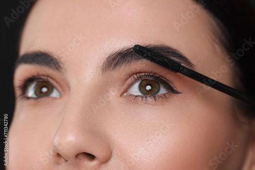 Beautiful young woman applying mascara on black background, closeup