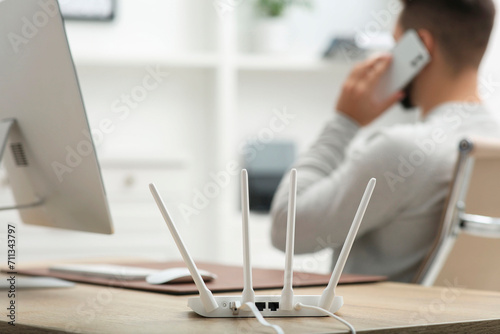 Fotografie Man talking on smartphone while working at wooden table indoors, focus on Wi-Fi