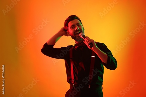 Emotional man with microphone singing in neon lights on orange background