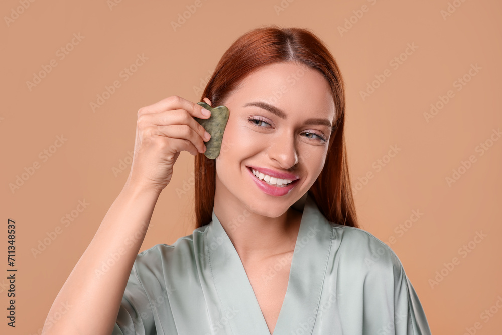 Young woman massaging her face with jade gua sha tool on pale orange background Young woman massaging her face with jade gua sha tool on pale orange background