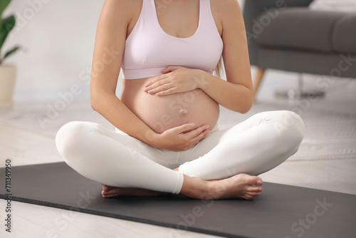 Pregnant woman sitting on yoga mat at home, closeup