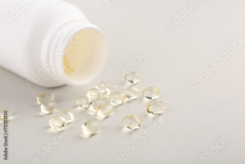 Vitamin capsules and bottle on light grey background, closeup. Space for text