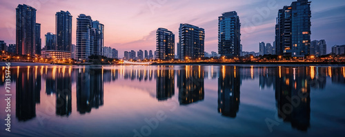 A panoramic view of a tranquil waterfront cityscape at dusk with skyscrapers reflected in the calm water under a pastel sky.