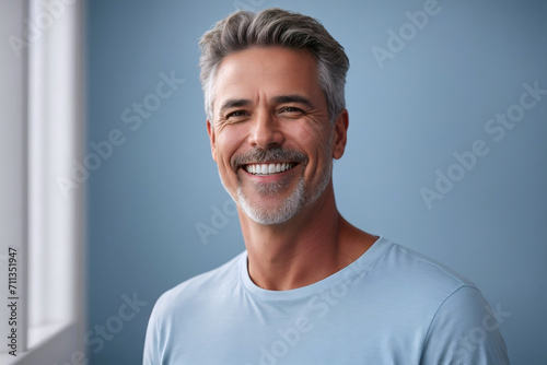 Middle aged man with perfect, clean, white teeth smile on solid blue background for dentist advertisement.
