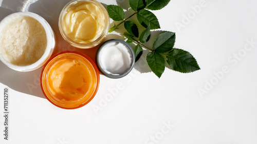 Skincare cosmetics. Composition of a different containers with natural herbal moisturising products scrub, cream, peeling, green tea tree lotion and chea butter, top view, white background