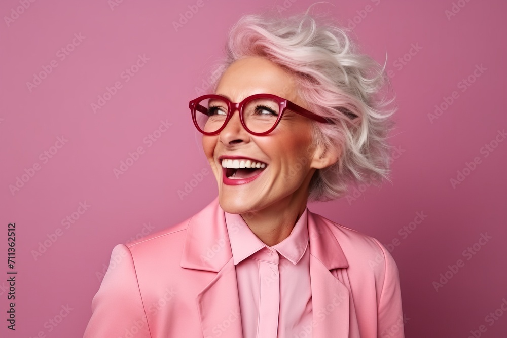 Portrait of a happy senior woman with pink hair and glasses over pink background