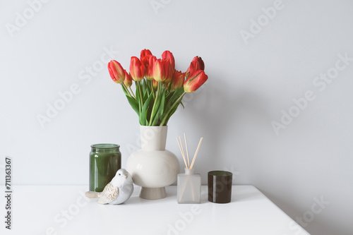 International woman's day concept. Spring home decorations with bouquet of red tulips, candles and aroma diffusion sticks. Cozy lifestyle, seasonal decor