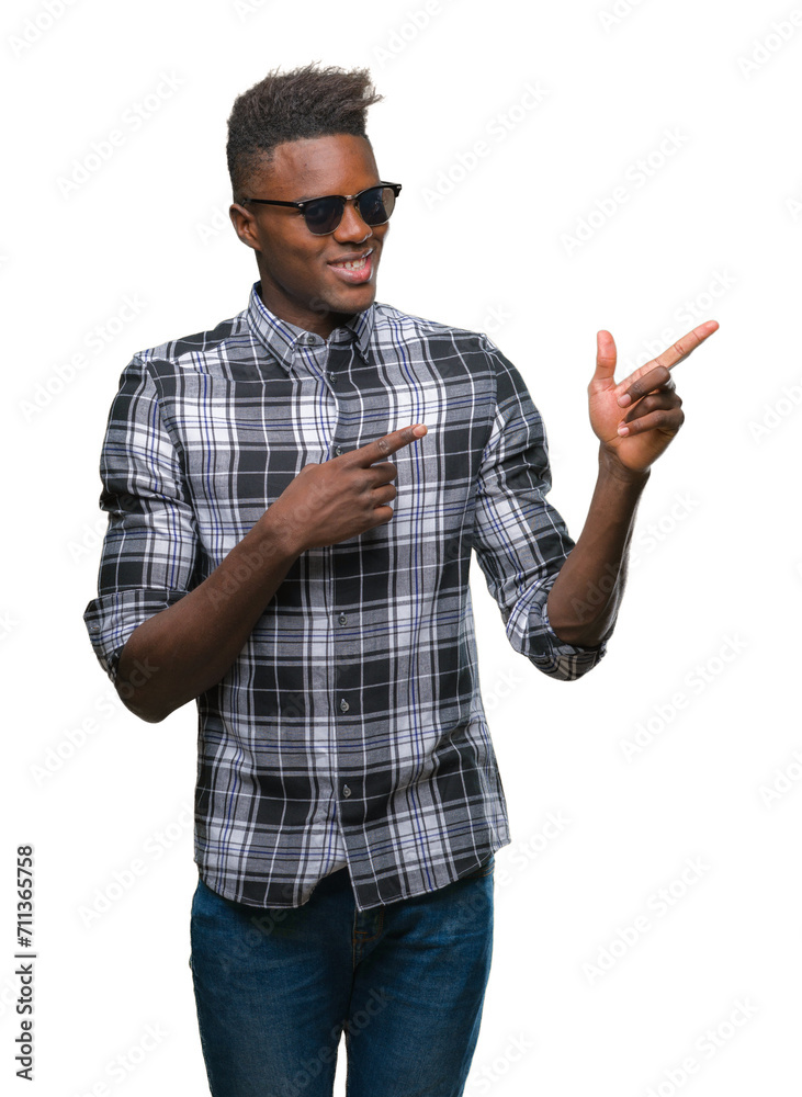 Young african american man wearing sunglasses over isolated background smiling and looking at the camera pointing with two hands and fingers to the side. Young african american man wearing sunglasses over isolated background smiling and looking at the camera pointing with two hands and fingers to the side.