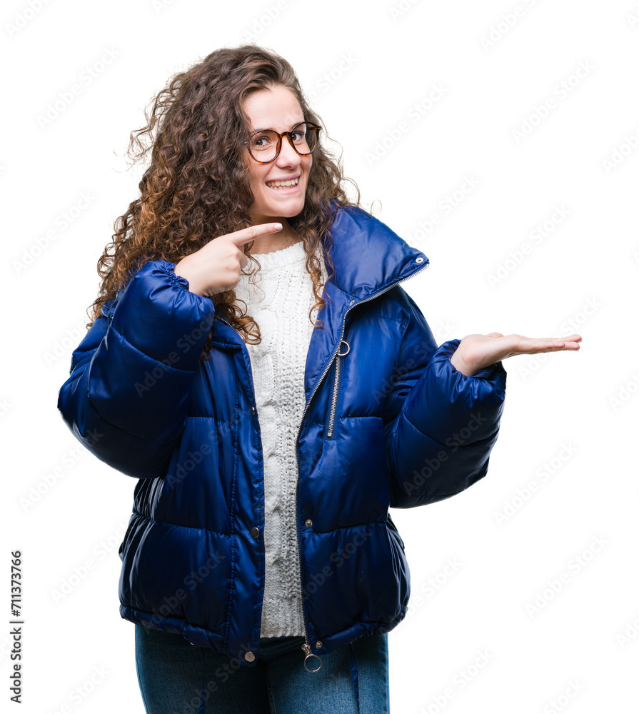 Φωτογραφία Beautiful young brunette curly hair girl wearing winter coat, glasses and sweater over isolated background amazed and smiling to the camera while presenting with hand and pointing with finger