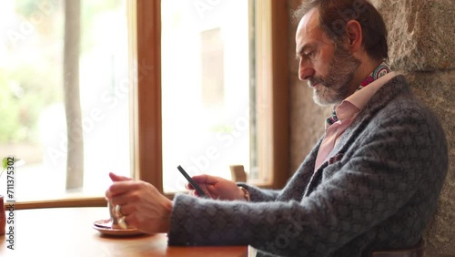 Adult man connected to social networks with mobile phone while calmly drinking coffeesitting in a cafe photo