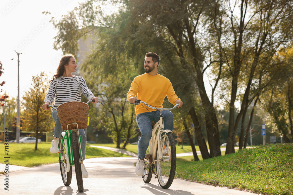 Beautiful young couple riding bicycles in park, space for text Beautiful young couple riding bicycles in park, space for text