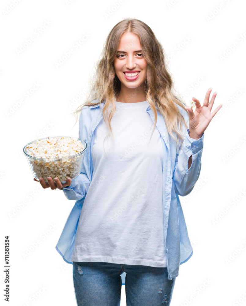 Beautiful young blonde woman eating popcorn over isolated background with a happy face standing and smiling with a confident smile showing teeth