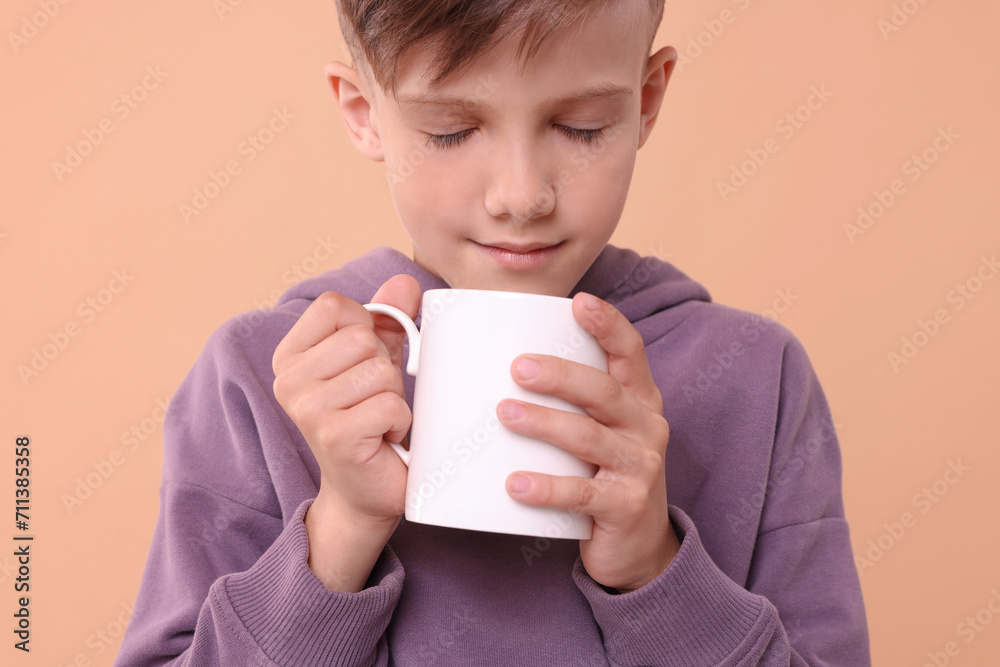 Cute boy with white ceramic mug on beige background