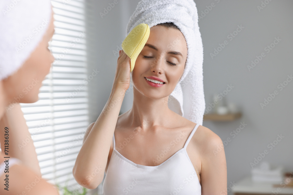 Happy young woman washing her face with sponge near mirror in bathroom Happy young woman washing her face with sponge near mirror in bathroom